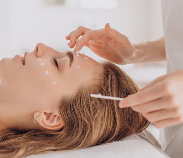 Tratamiento efecto Botox woman lying with eyes closed during a facial treatment as cream dots are applied to her face with a cotton swab by an esthetician.