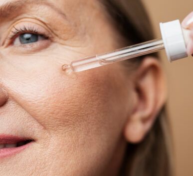 close-up of a woman applying eye serum with a dropper near her eye, focusing on the skin around the eye area.