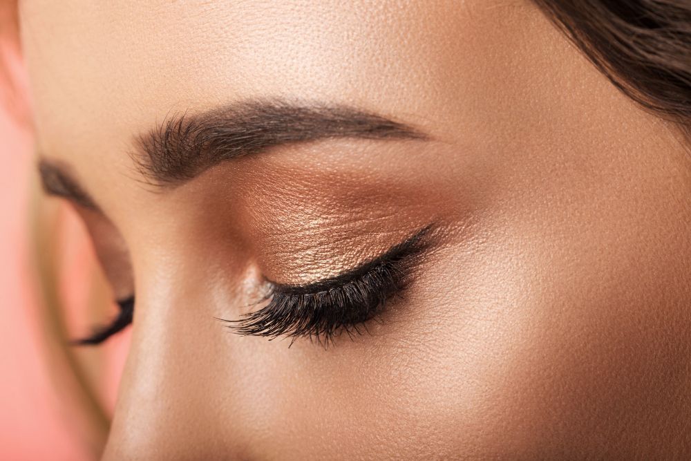 Close-up of a woman's closed eye with shimmery bronze eyeshadow and long lashes.