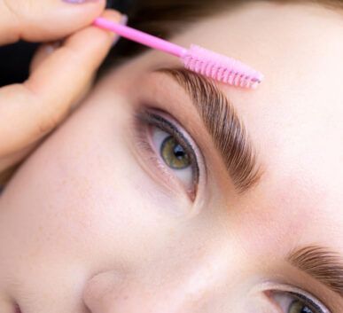 Close-up of a person using a pink eyebrow spoolie to brush their eyebrow hairs above the eye.
