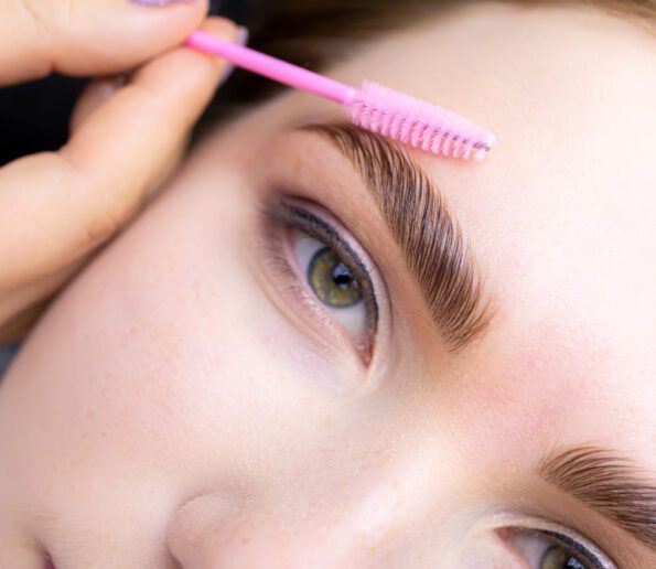 micropigmentación en Las Palmas close-up of a person using a pink eyebrow spoolie to brush their eyebrow hairs above the eye.