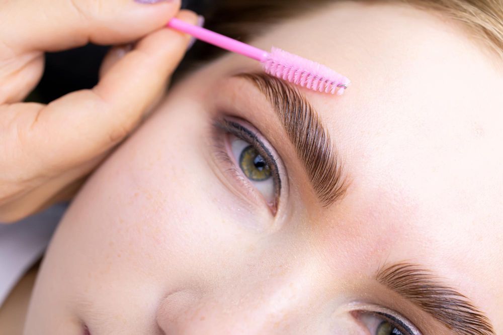 Close-up of a person using a pink eyebrow spoolie to brush their eyebrow hairs above the eye.