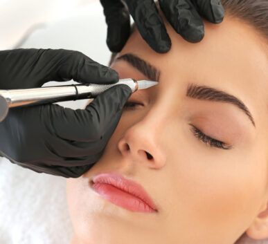 close-up of a beauty professional in black gloves using a pen-like device on a client’s closed eye during a cosmetic eye treatment.