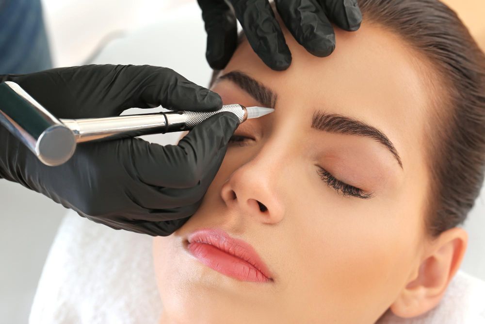 Close-up of a beauty professional in black gloves using a pen-like device on a client’s closed eye during a cosmetic eye treatment.