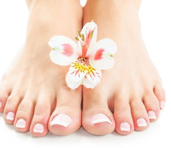 pedicura (4) pedicure-ready feet with white nail polish and a white orchid-like flower resting between the toes on a white background.