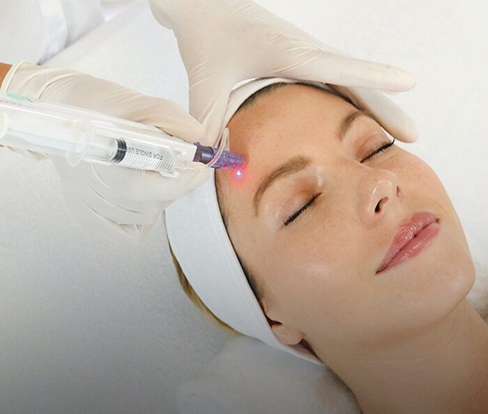 Woman with eyes closed receives laser facial treatment as a clinician in gloves applies a purple laser near her temple.
