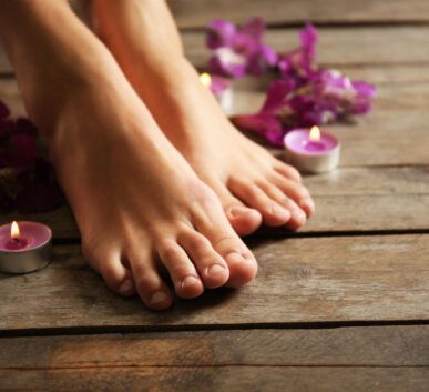pair of bare feet resting on a wooden floor surrounded by pink candles and purple flowers for a spa setting.