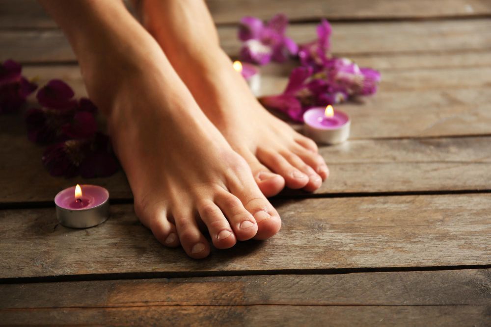 Pair of bare feet resting on a wooden floor surrounded by pink candles and purple flowers for a spa setting.