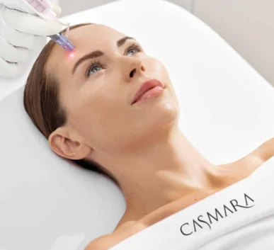 woman receiving a facial laser treatment on the forehead, with a clinician's gloved hand holding a laser device.