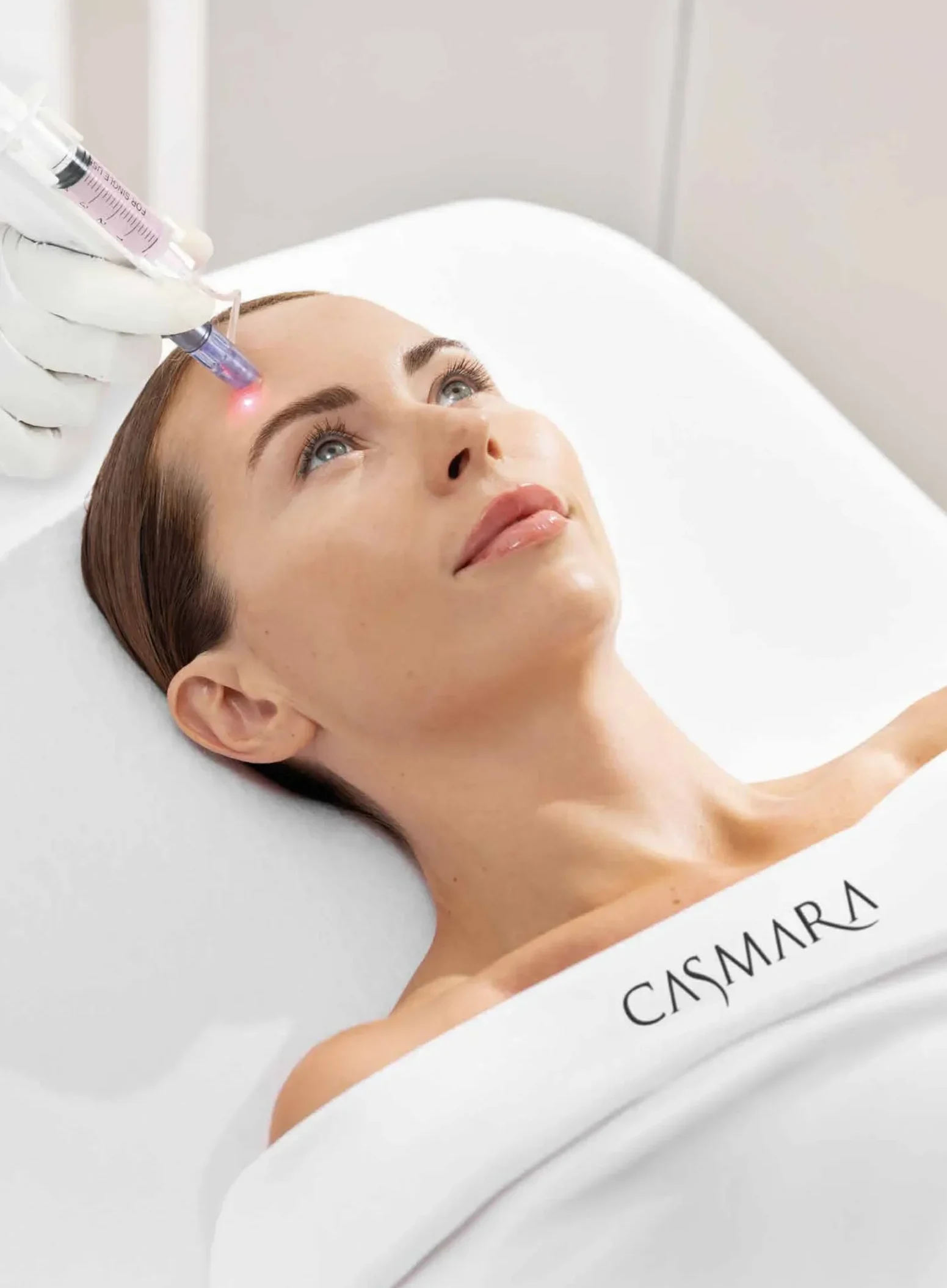 Woman receiving a facial laser treatment on the forehead, with a clinician's gloved hand holding a laser device.